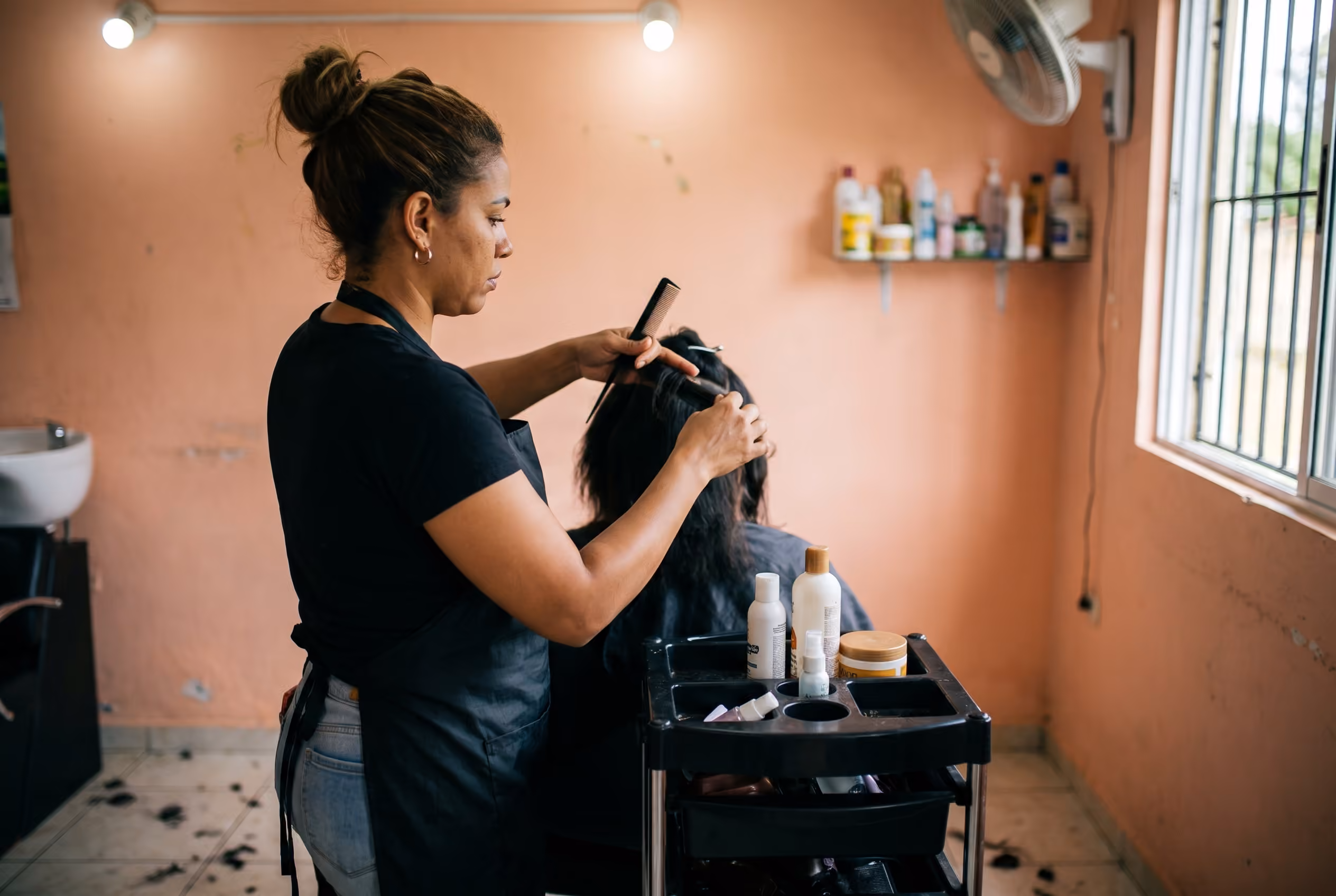 Estilista seccionando el cabello de una clienta en un salón, ambas concentradas en el trabajo.